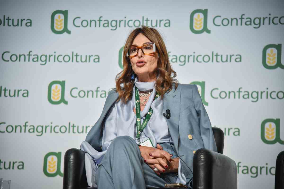 La Ministra del Turismo, Daniela Santanché, seduta ed elegantemente vestita durante un evento di Confagricoltura con tabellone con logo Confagricoltura sullo sfondo.